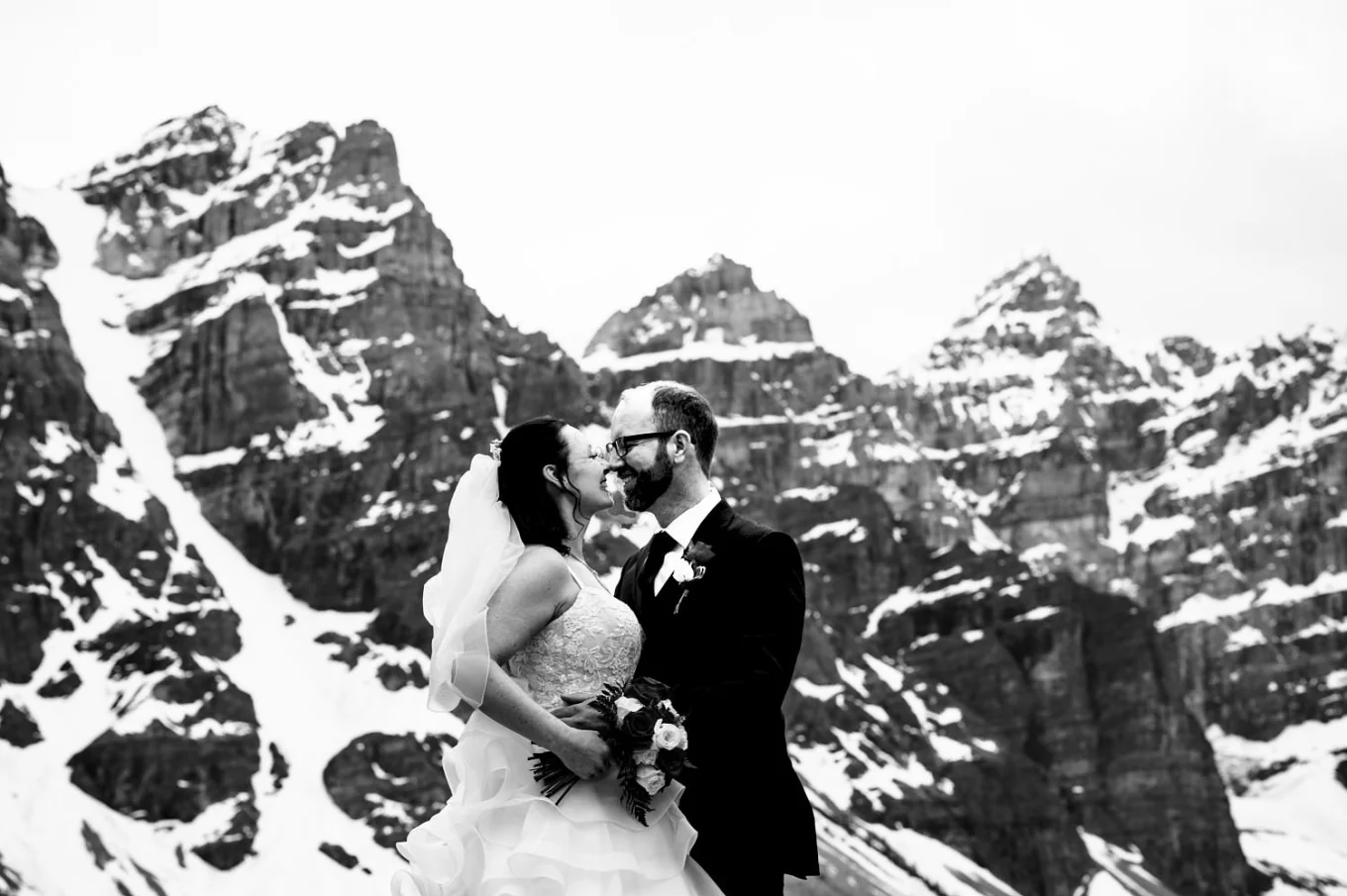 Newlyweds kiss. They use noses to kiss. Funny photography n black and white against mountains in Banff.