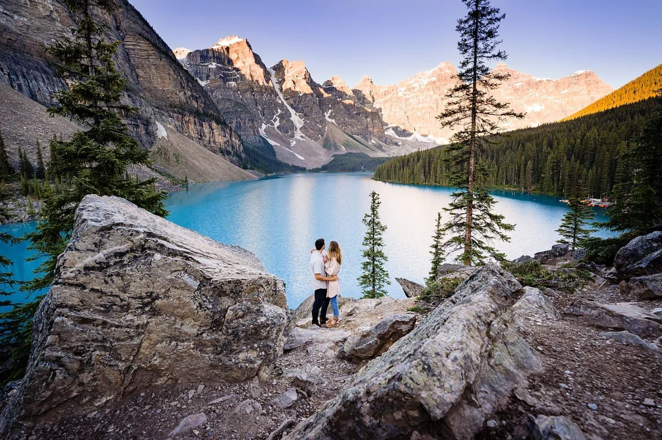Engagement portrait from Moraine Lake of hugging couple who look at the lake.
