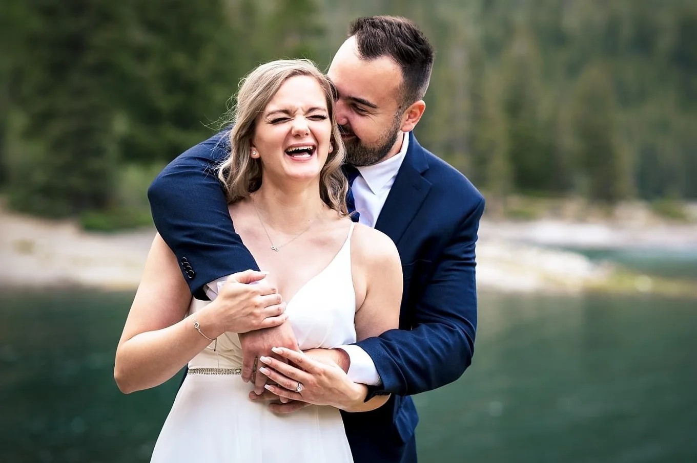 Groom stands behind bride and whisper something funny to her ear. They both lough,