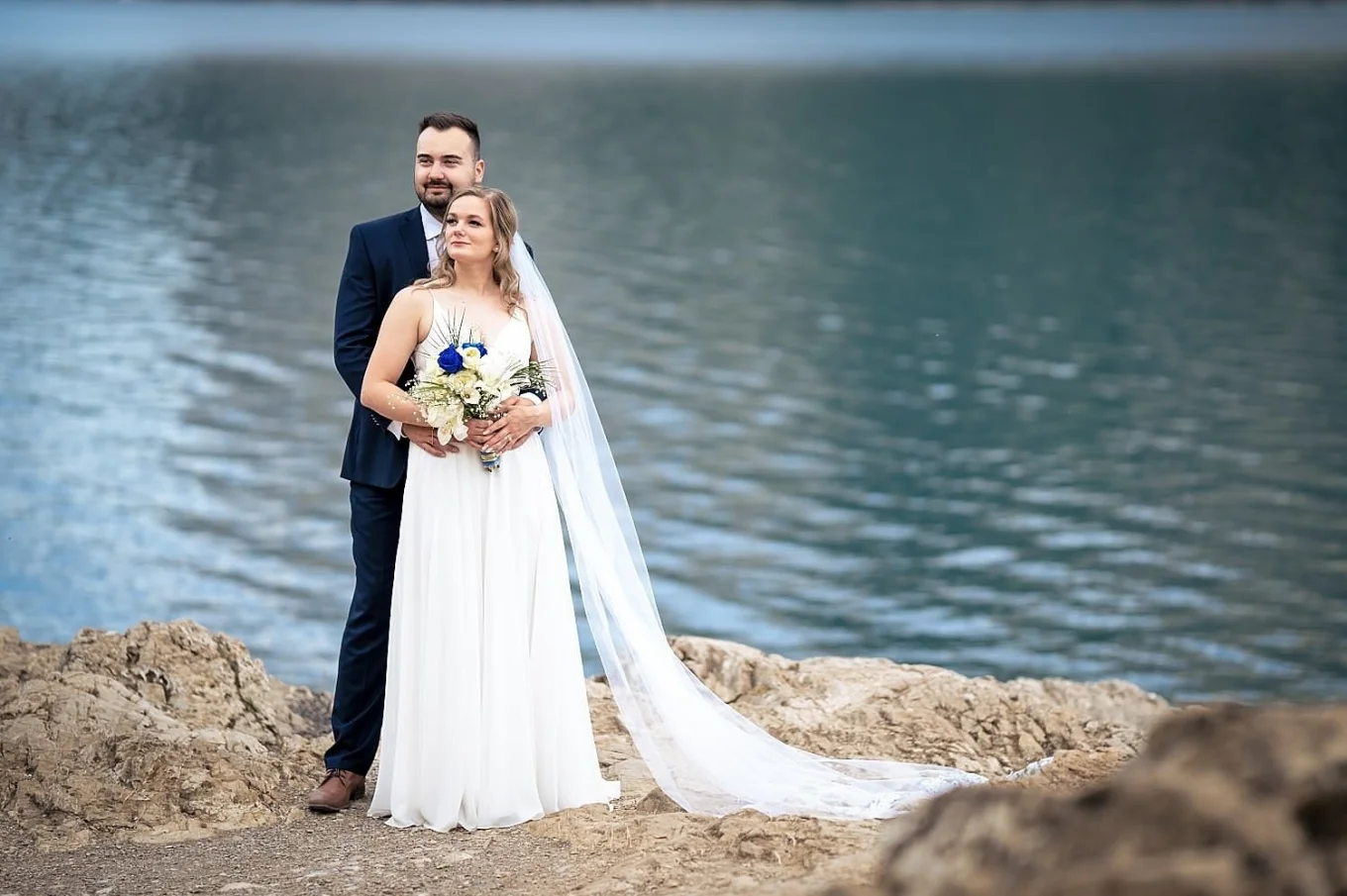 Wedding Portrait by the Minnewanka Lake. Groom hugs the bride from behind and they both look at the same direction.