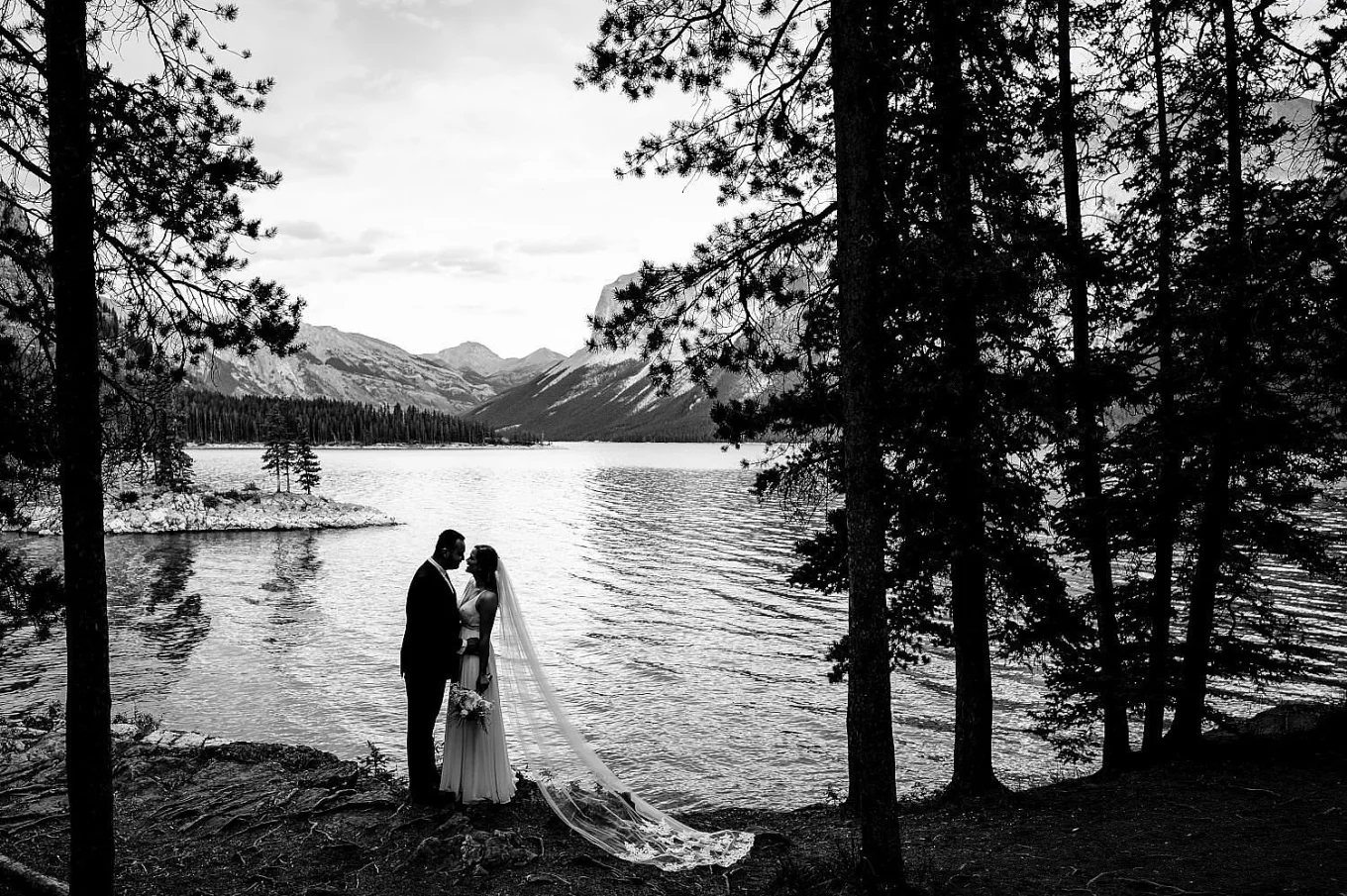 Bride and facing each other an touches their noses. Stunning wedding portrait by the lake in black and white