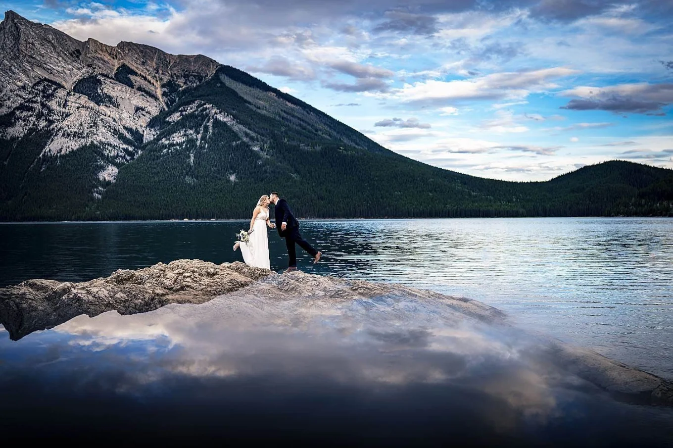 Bride abd grom share a kiss an the huge island by the Minnewanka Lake in Banff