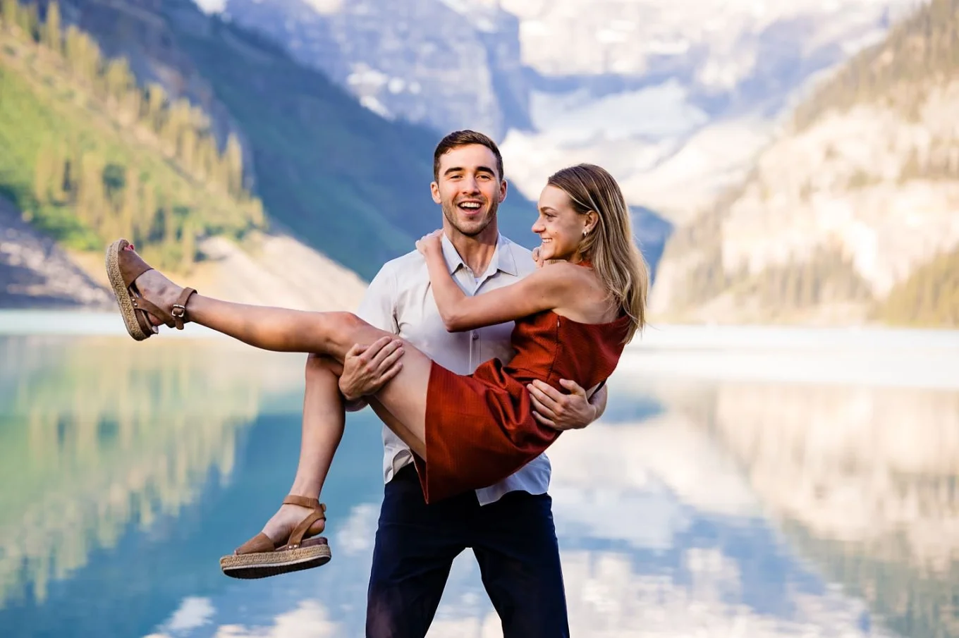 The men is caring his fiancee on his hands during fun Banff Engagement at Lake Louise.
