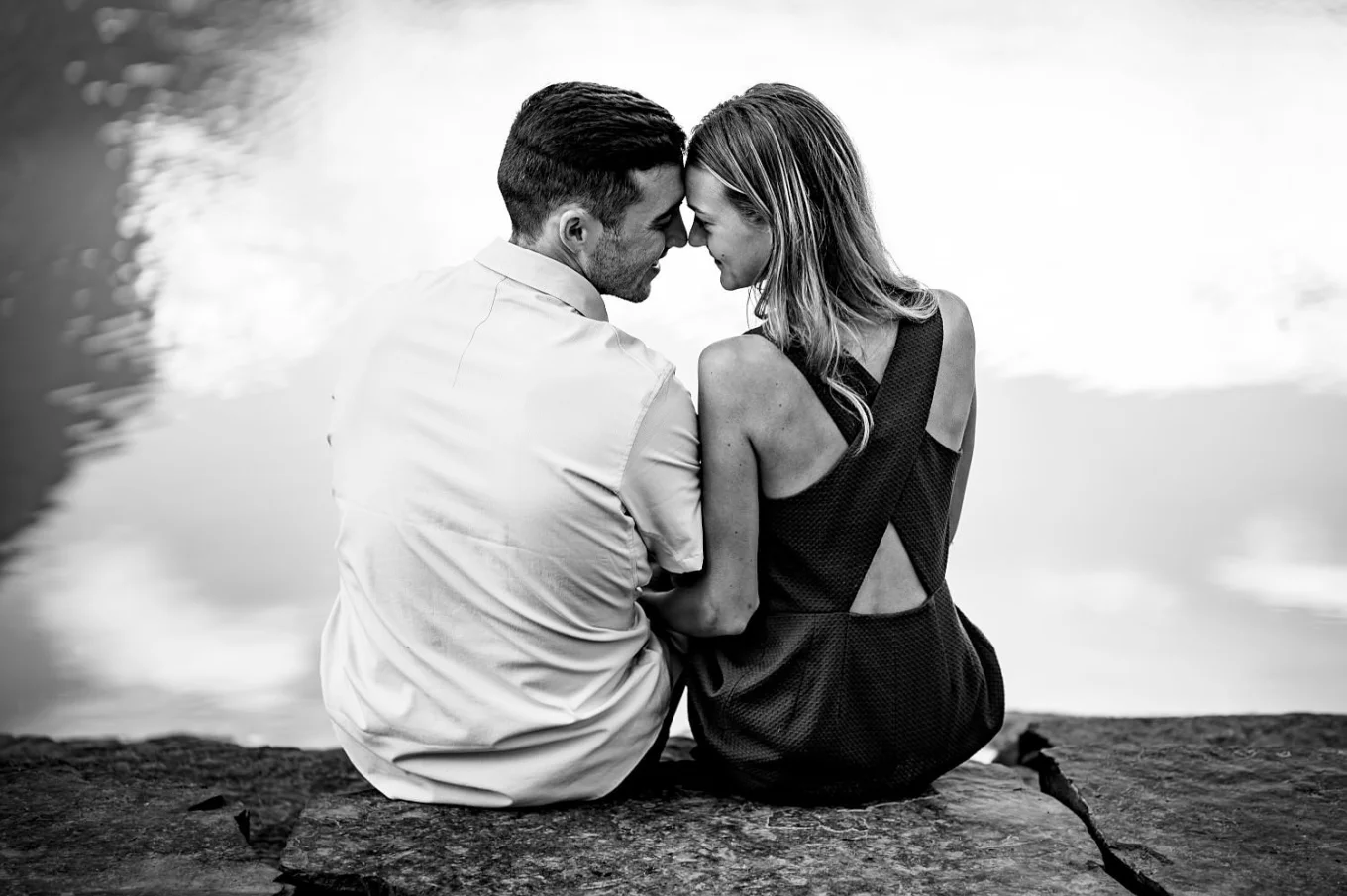 Cute photograph of engaged couple sitting by the lake ,