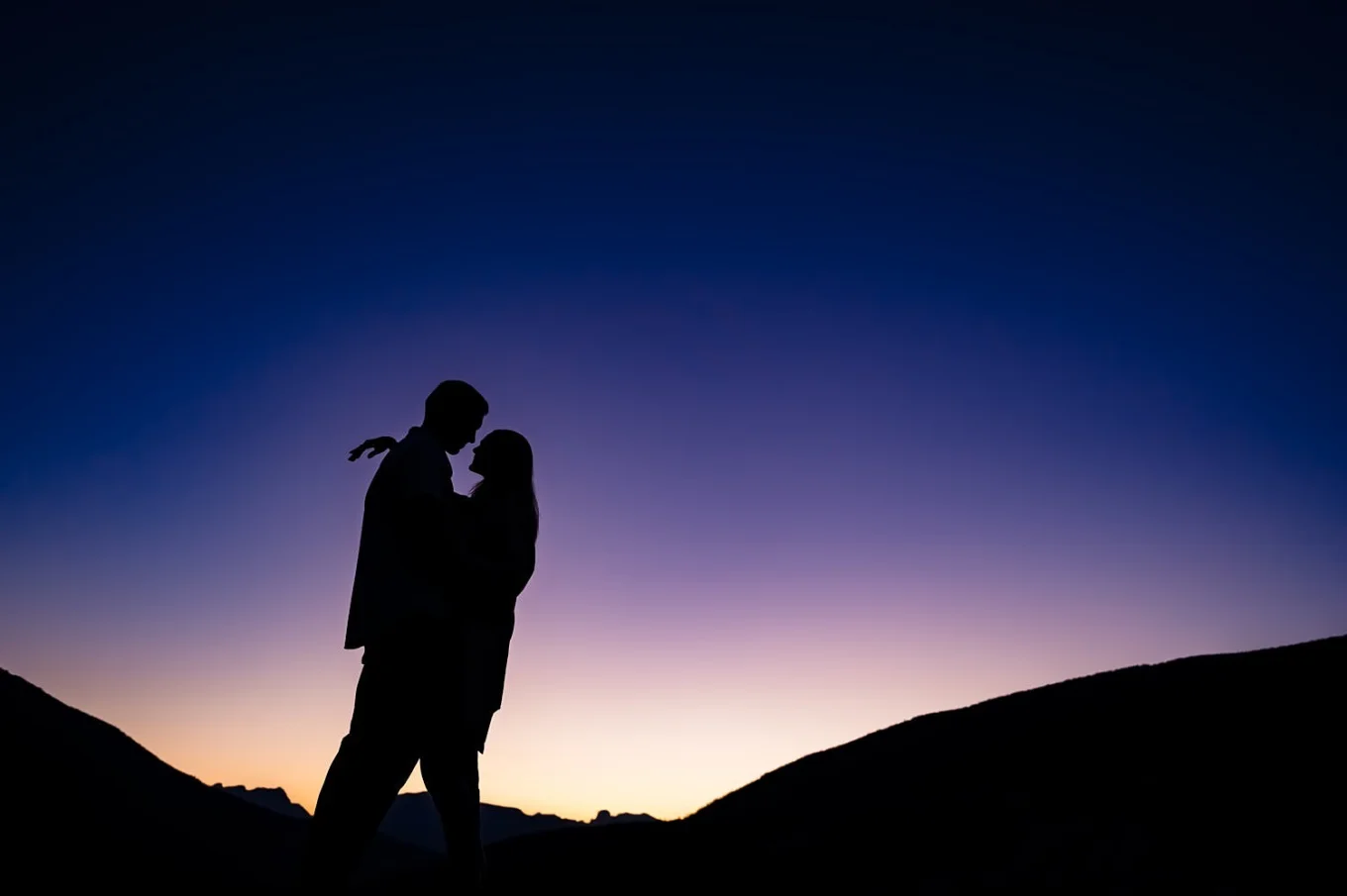 Engaged couple pose outside in Banff against purple and orange sky.