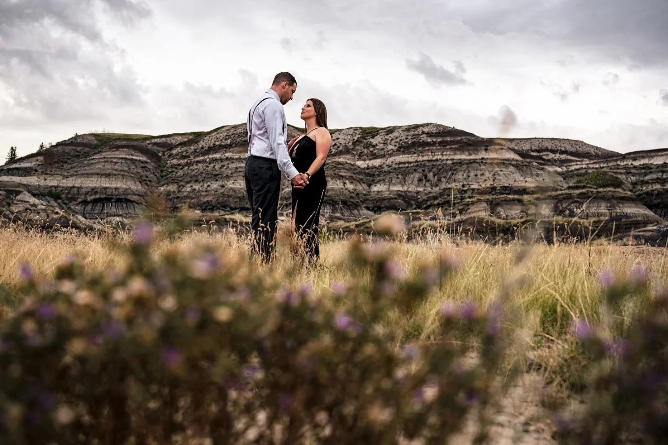 Men and woman holds their hands and look deeply into each others eyes during after wedding photo session at Horseshoe Canyon in Alberta, Canada.