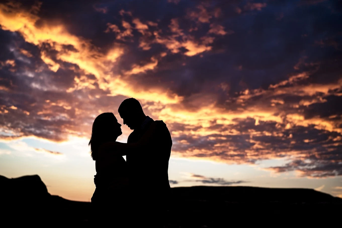 Silhouetted engaged couple against colourful sunrise