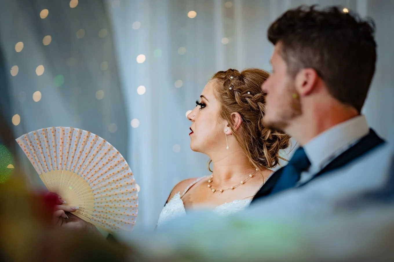 Bride and groom on the reception. Bride cools herself down with a hand fan.
