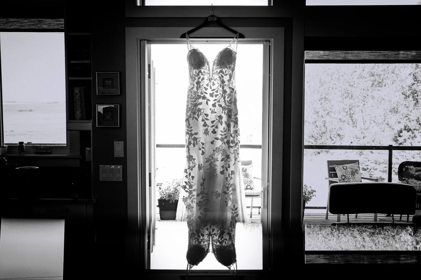 Amazing black and white photograph of a wedding dress hanging on the window frame.