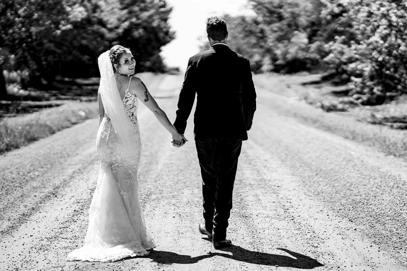 Bride and groom walk on the dirt road in Calgary. Bride looks at the camera.