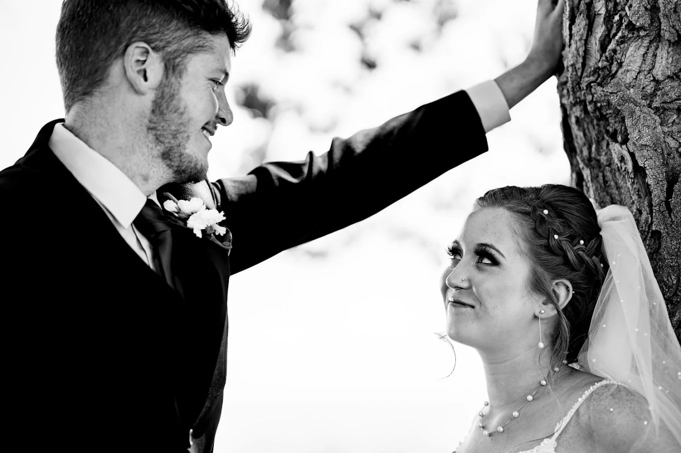 bride lean over a tree and the groom put his hand on the tree looking deeply into bride's eyes