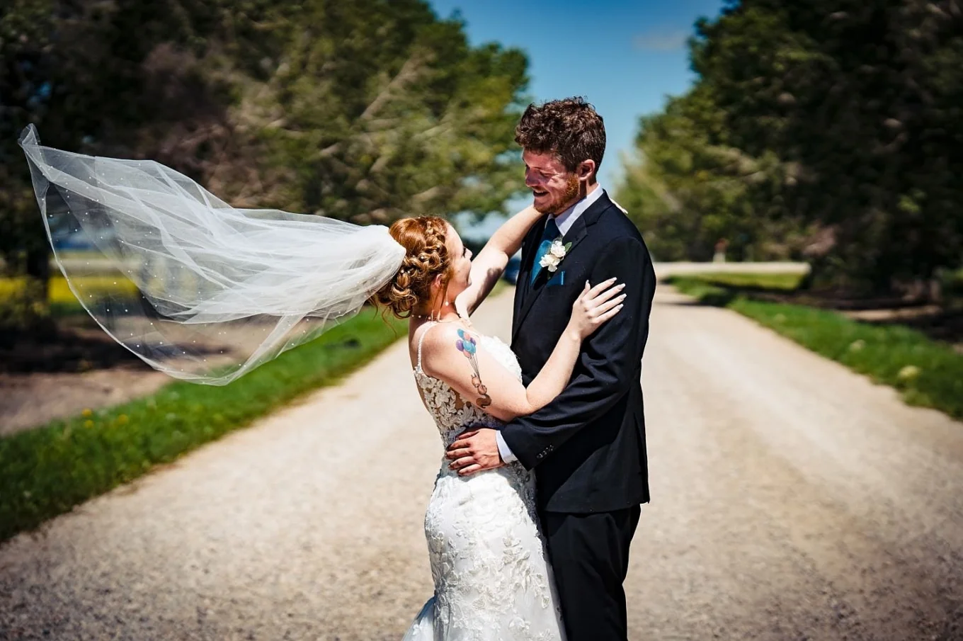 Bride and room in a hug, looking at each other. Bride's veil fly with the wind.