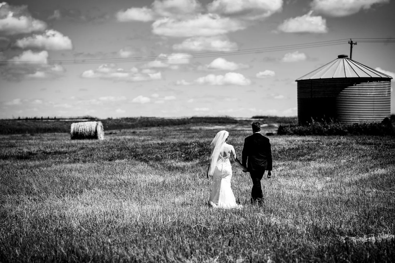 Black and white wedding photograph of newlyweds walking on the filed outside Calgary.
