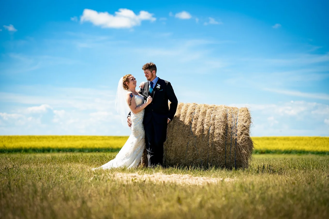 Groom lean against hay cone and the bride is next to him looking deeply into his eyes.