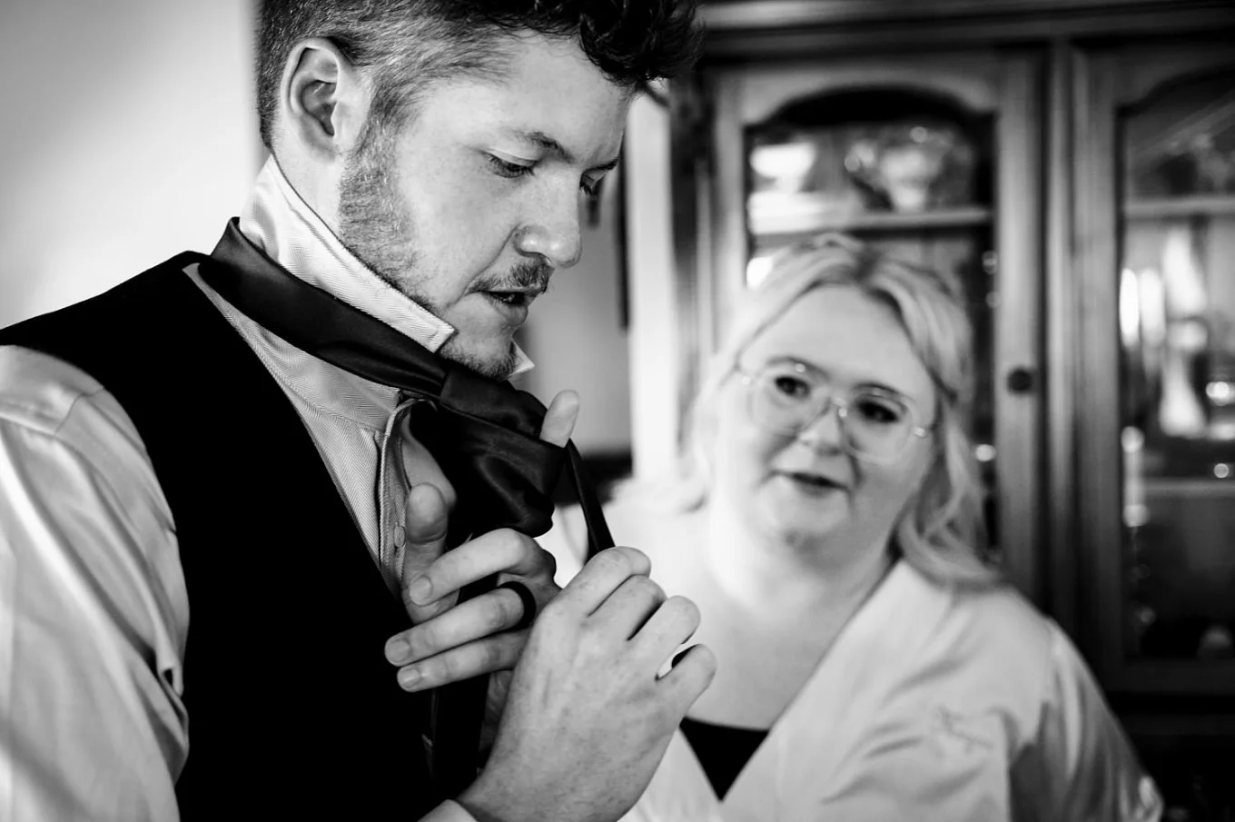 Groom tries to tie his tie. His friend look at him.