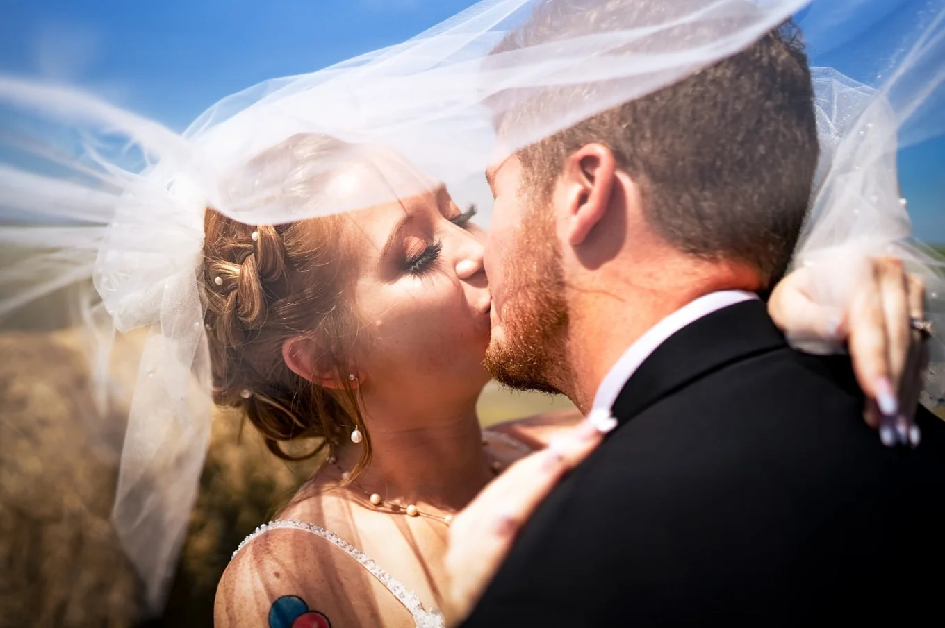 Bride and groom share a kiss under a veil.