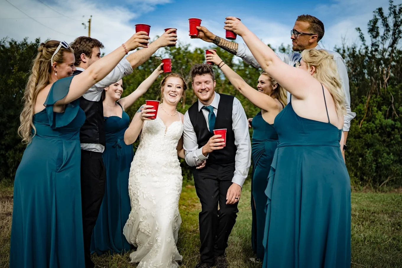Bridal party creates a tunnel with their hands and drinks in their hands. Bride and groom walks through that tunnel.