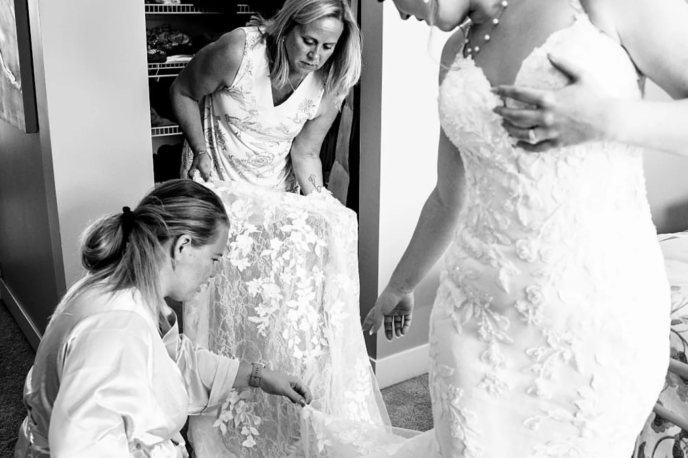 Bride's Mother and Bridesmaid help the bride with the wedding dress. Brides points out on the buttons on her dress.