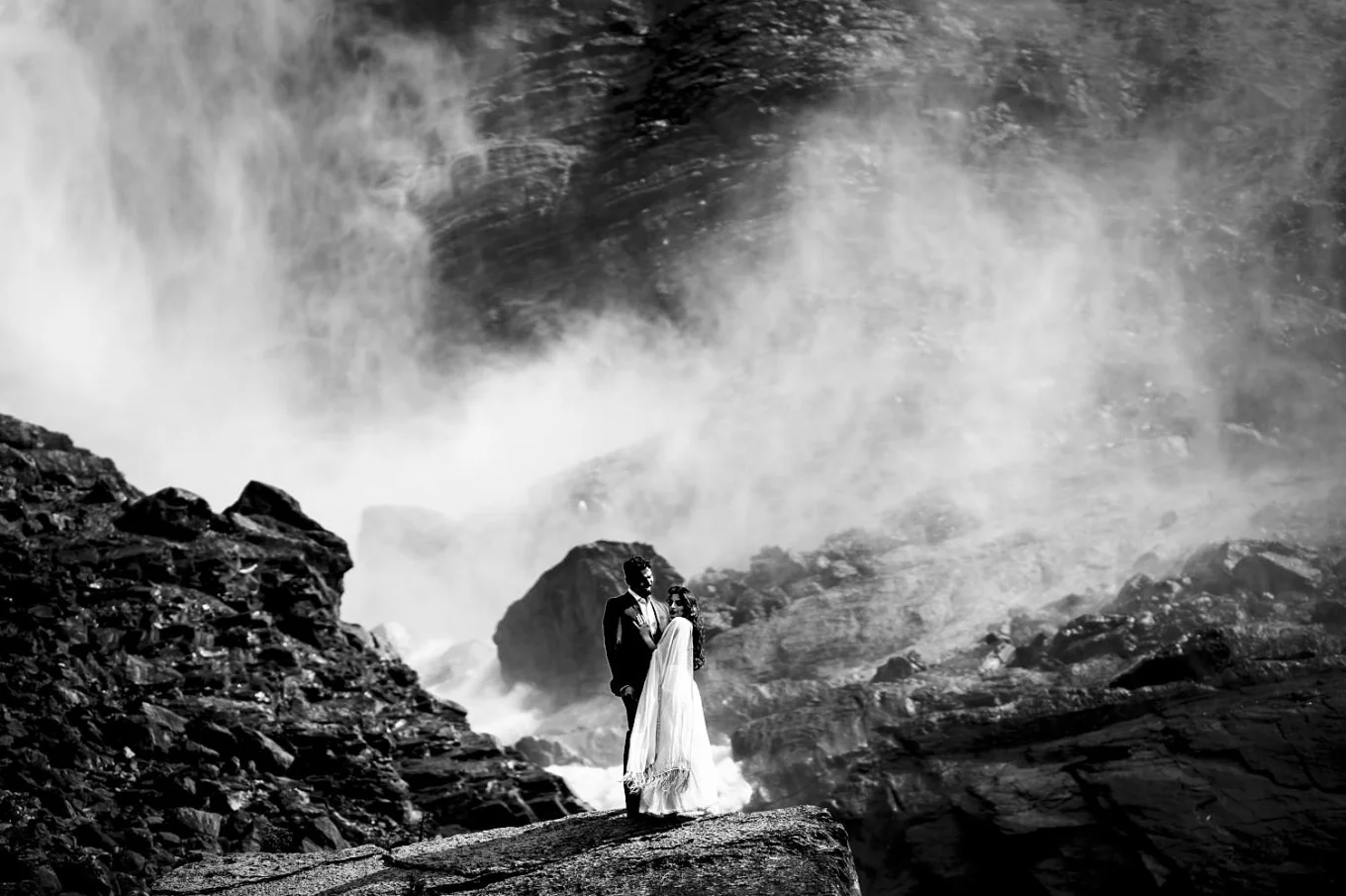 Engagement photo session at Takakkaw Falls in Canada with Indian couple. They are dressed in traditional outfits and hug each other.j