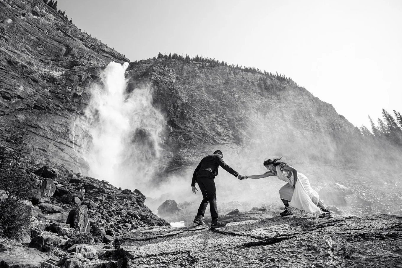 Man helps his fiance to fight strong wind at Takakkaw Falls.