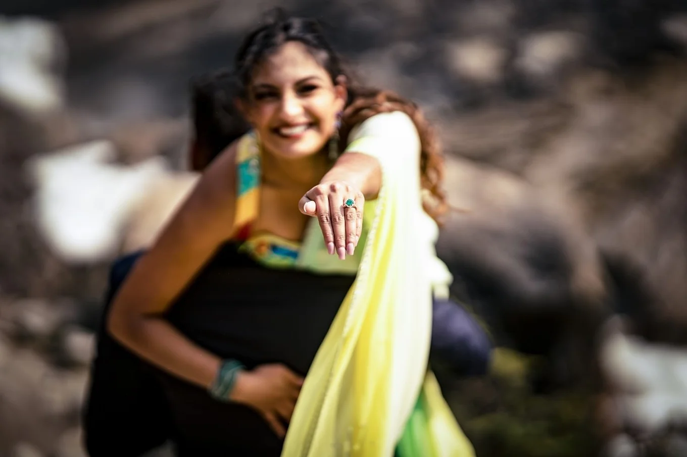 Beautiful Indian girl shows her engagement ring while her fiancee carry her on his shoulder.