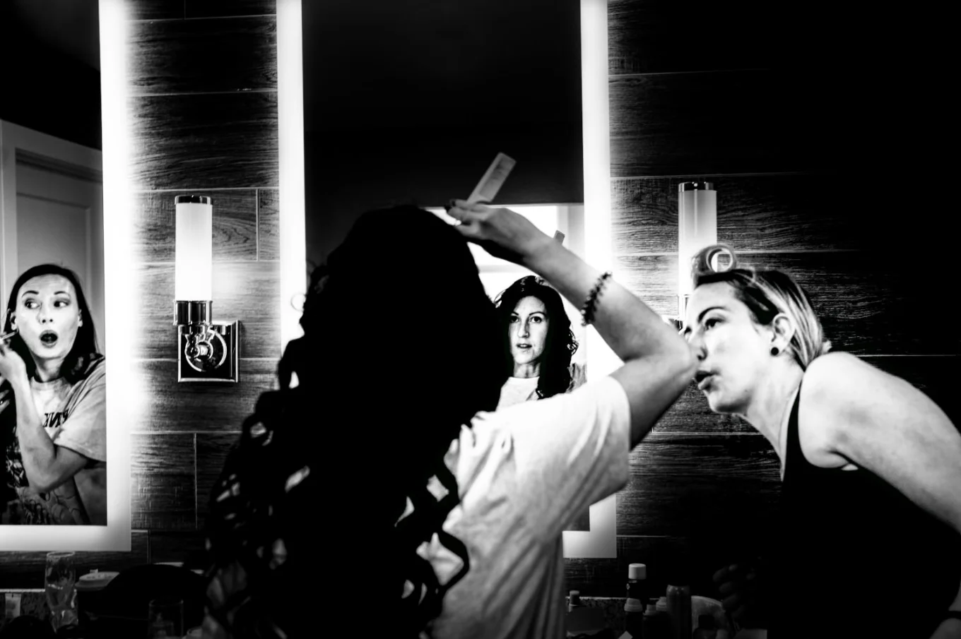 Bride fixing hair hair in the mirror while her friend look at her.