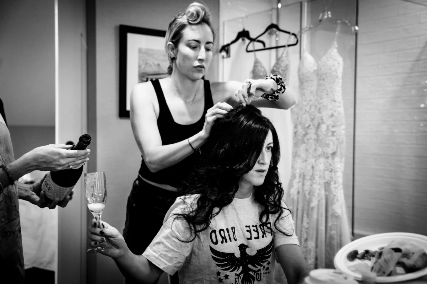 Bride is getting her hair done while her friend fill her glass with champagne