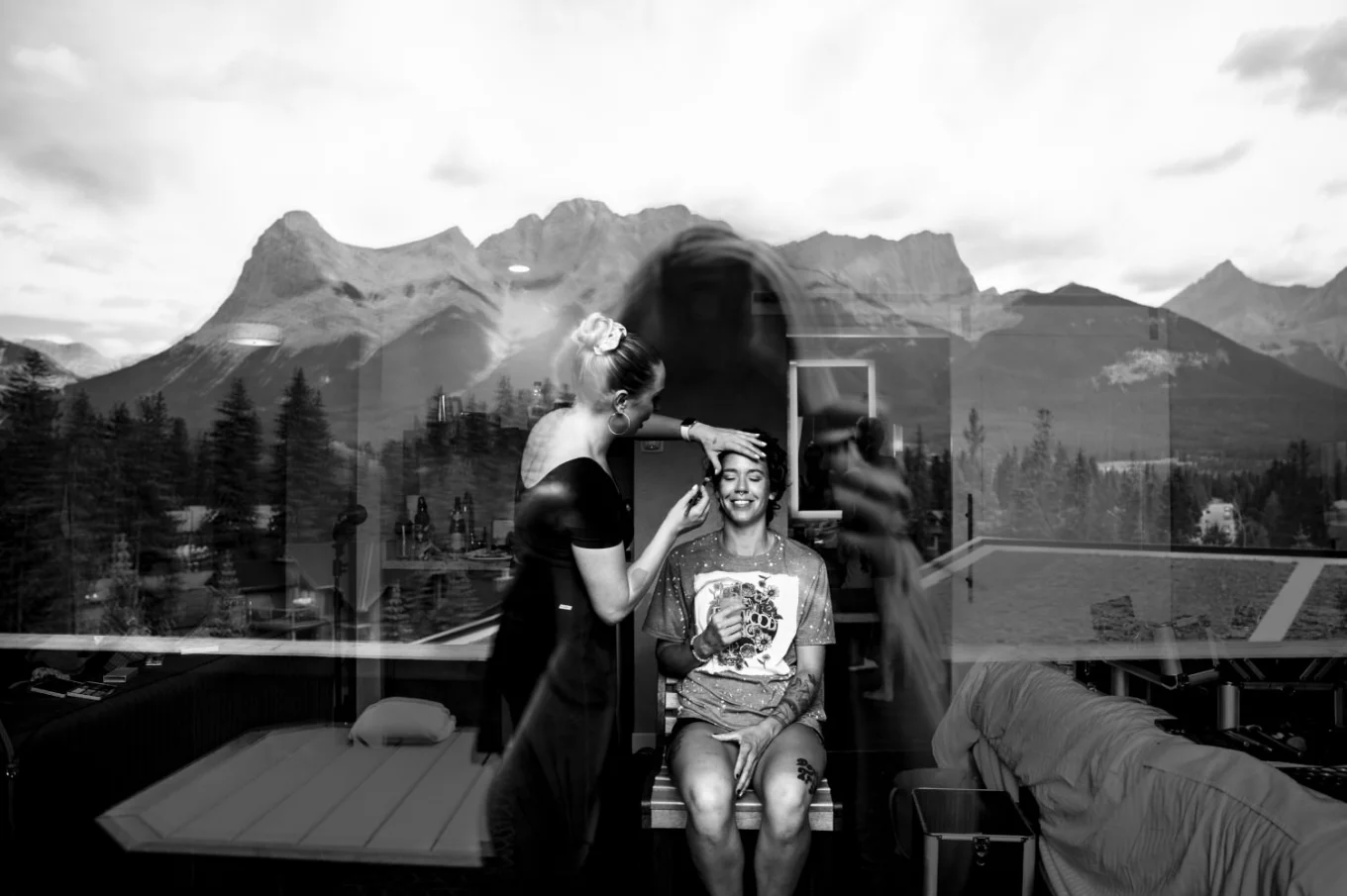 Black and white photograph of the bride getting her make up done . In the window amazing reflection of the Cnadian Rocky Mountains