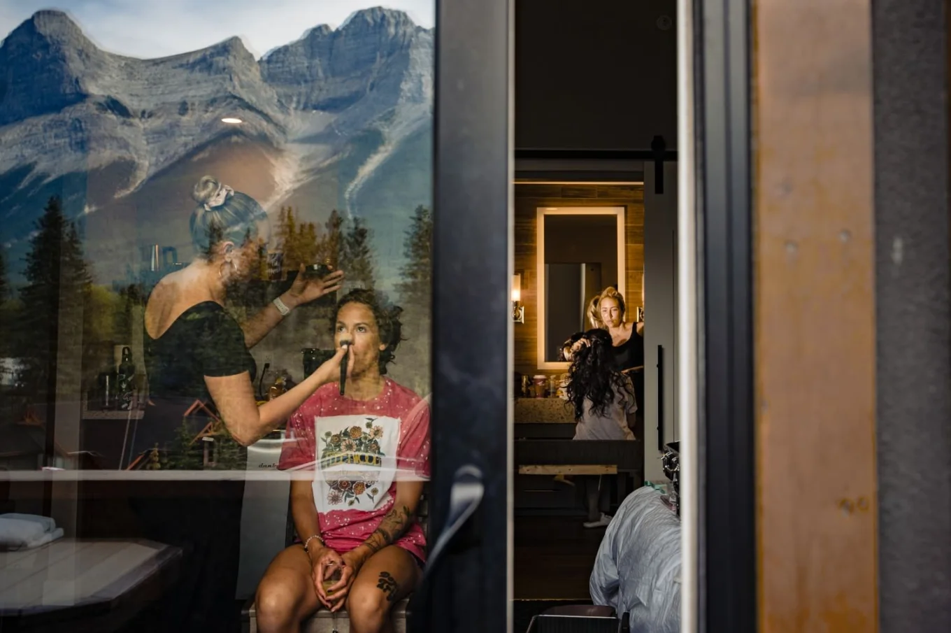 unique photograph of getting ready time before Banff Wedding . Bride and bridesmaid getting their hair and make up done. Photography through the window.