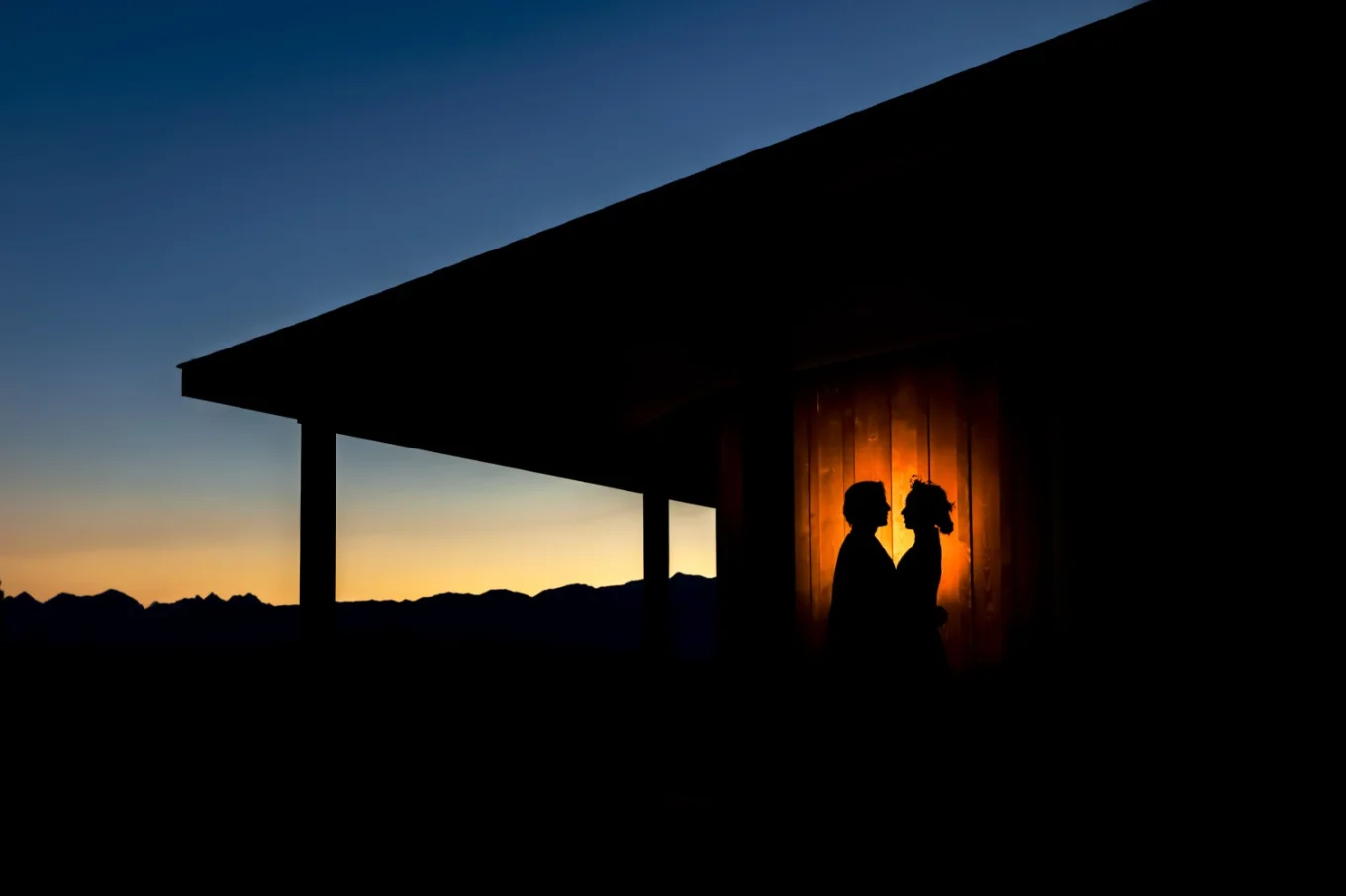 Creative photograph of silhouetted bride and groom against house in the Canadian Rocky Mountains.