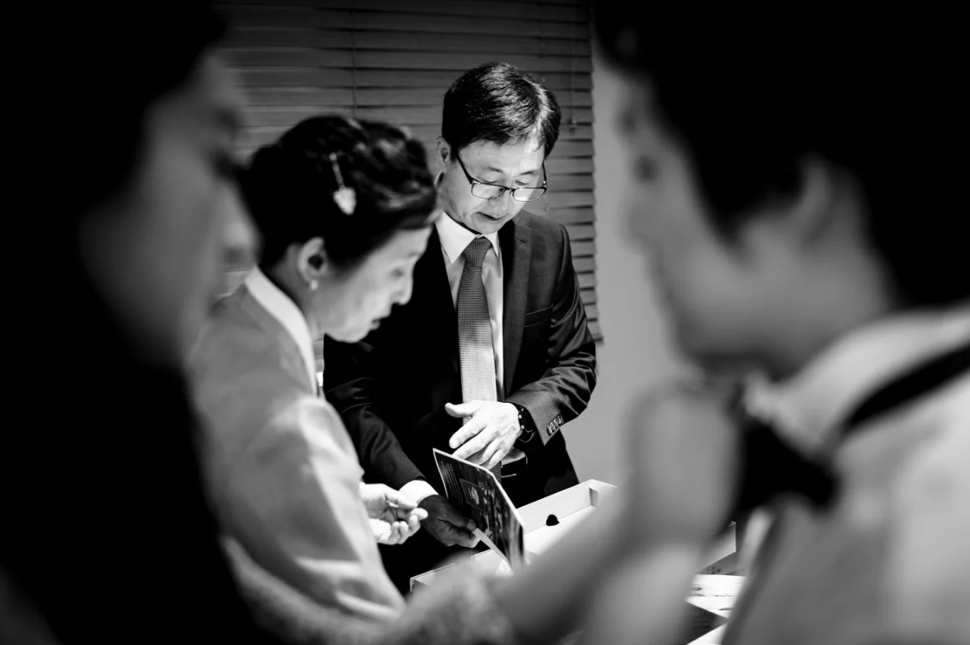 Getting ready time in black and white . Sister of the groom helps with his bow tie while parents look at the old photos.