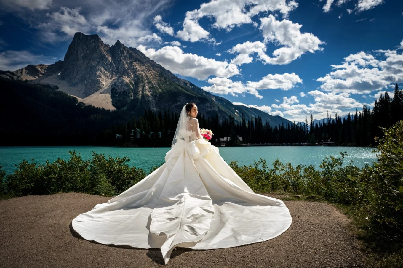 Bride wearing a huge , white wedding dress by the turquoise Emerald Lake.