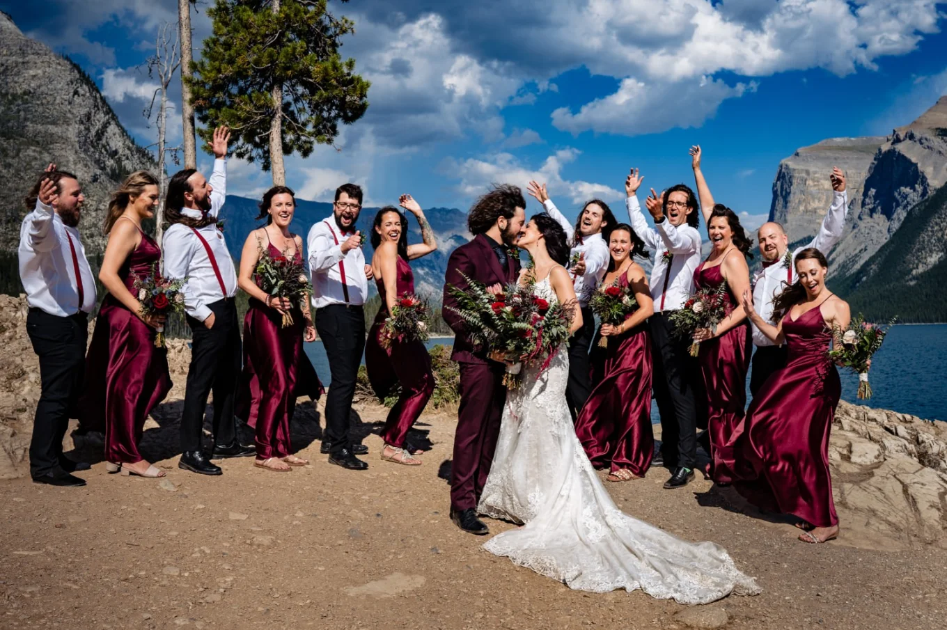 Bridal Party at Minnewanka Lake. Newlyweds share a kiss while bridal party cheer them.