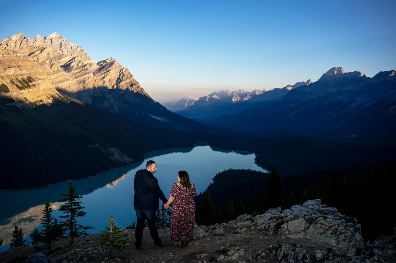 engaged couple hold their hands and look at each other on the top of the mountain at Peyto Lake in Banff.