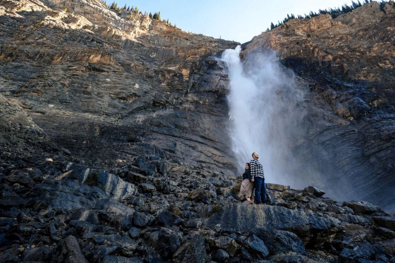 Man and lady stand back to back . Behind them powerful waterfall in Banff.
