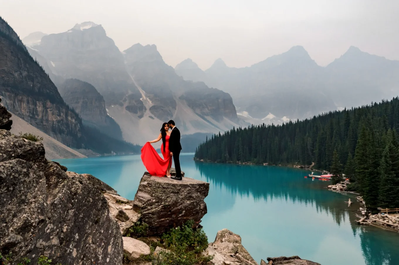 Calgary Wedding Photographer captured engaged couple standing on the rock at Moraine Lake during smoky morning.