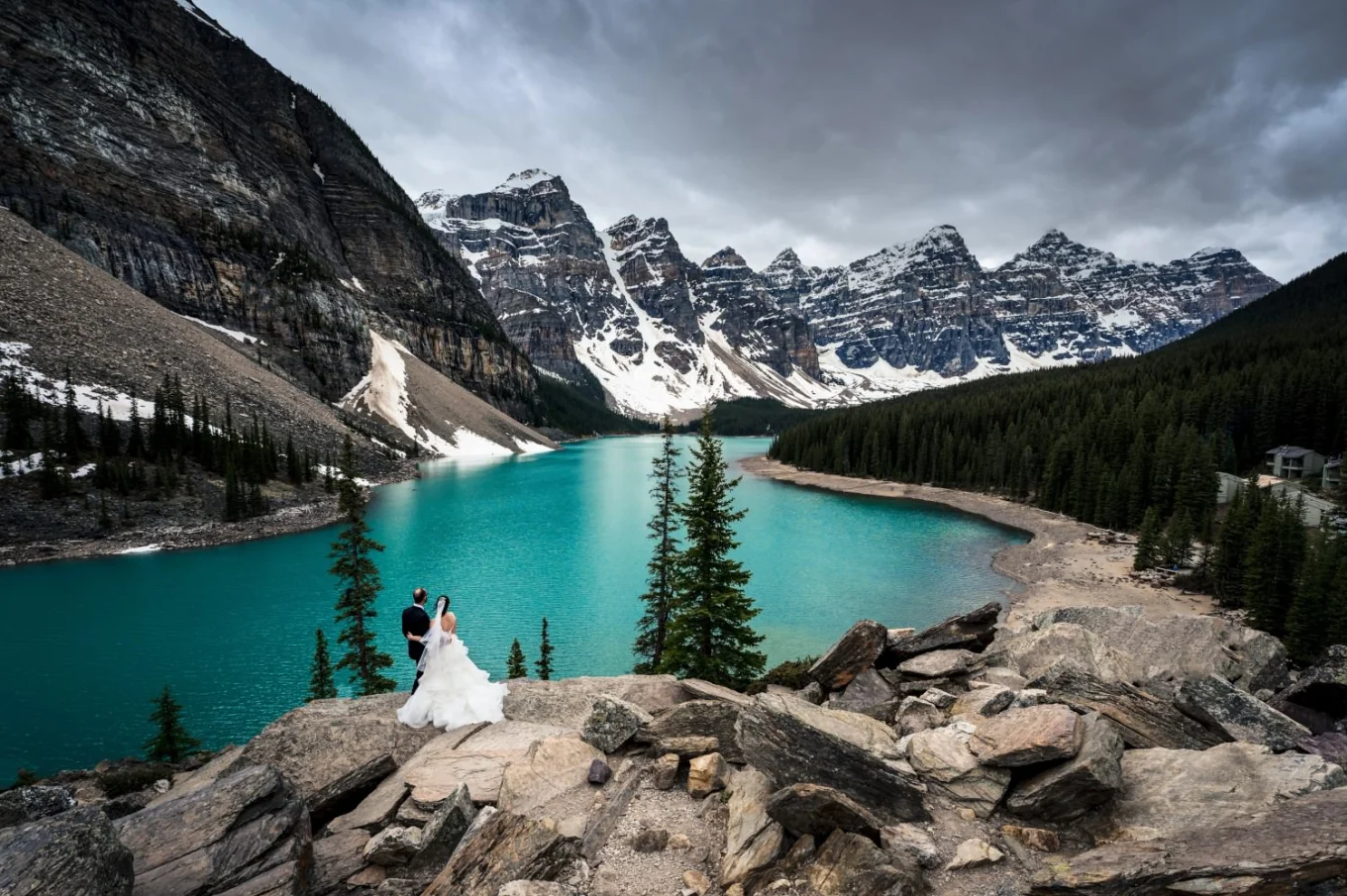 Banff Wedding Photography at Moraine Lake. Bride and groom stand in a hug watching magnificent turquoise c colour of the lake.