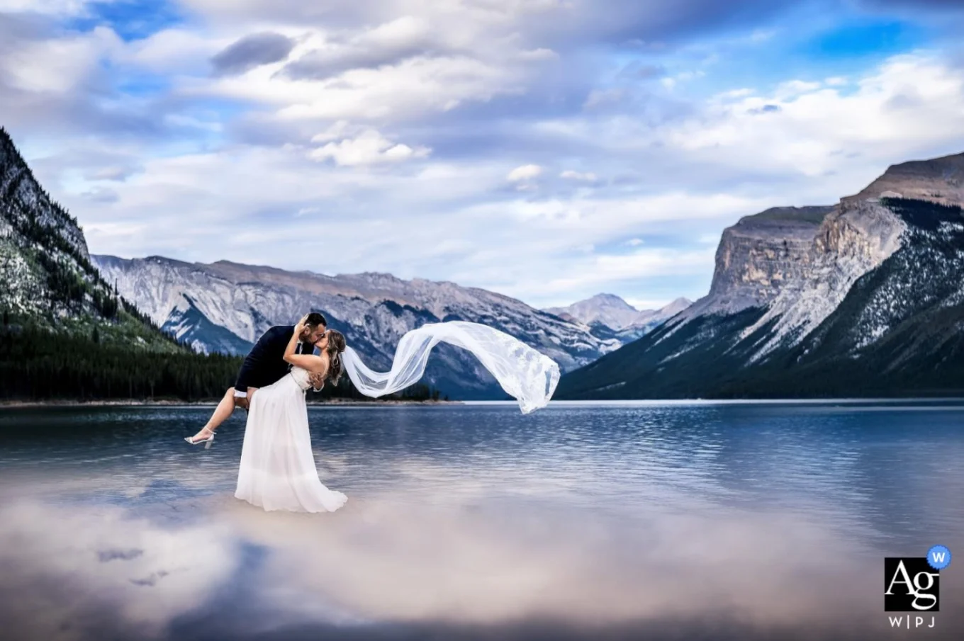 Newlyweds dance at Minnewanka Lake in Banff while her veil flies with the wind