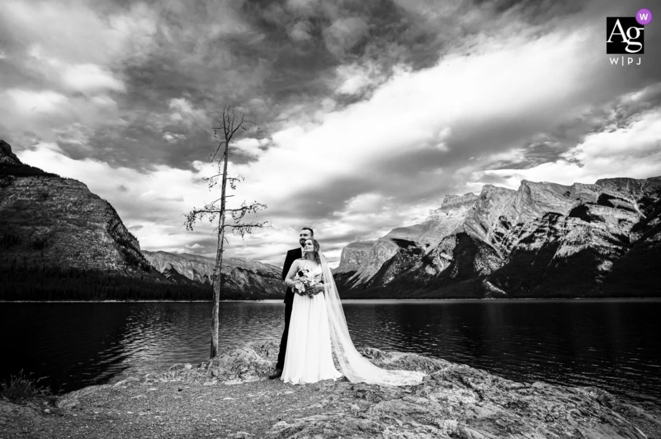 Groom hugging his wife at Minnewanka Lake. Photo taken by best Banff Wedding Photographer in black and white.