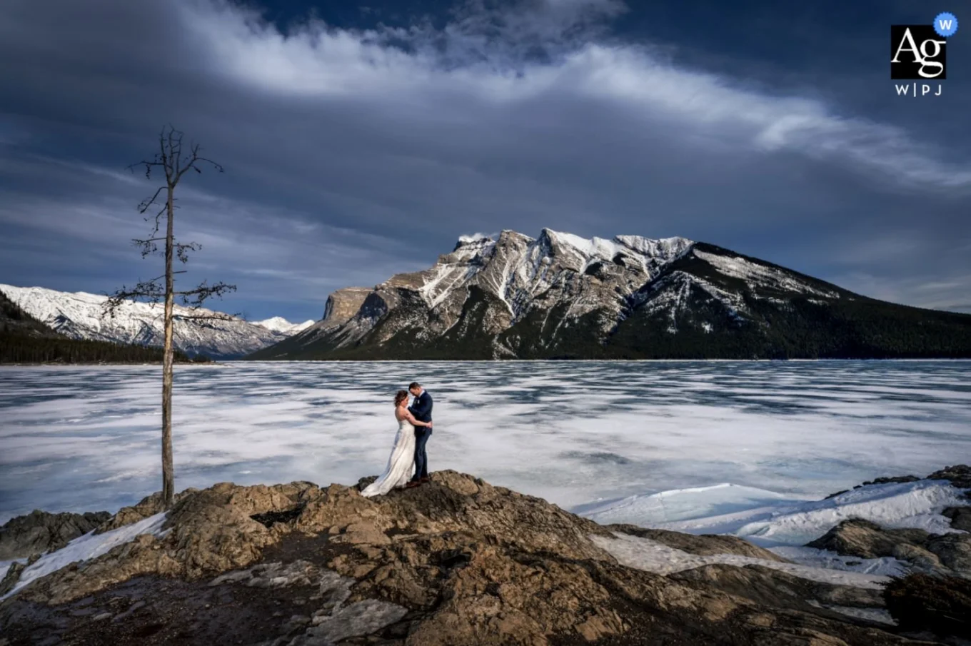 Winter Wedding Portrait Session takan by Banff Wedding Photographer of bride and groom in a hug at frozen Minnewanka Lake.