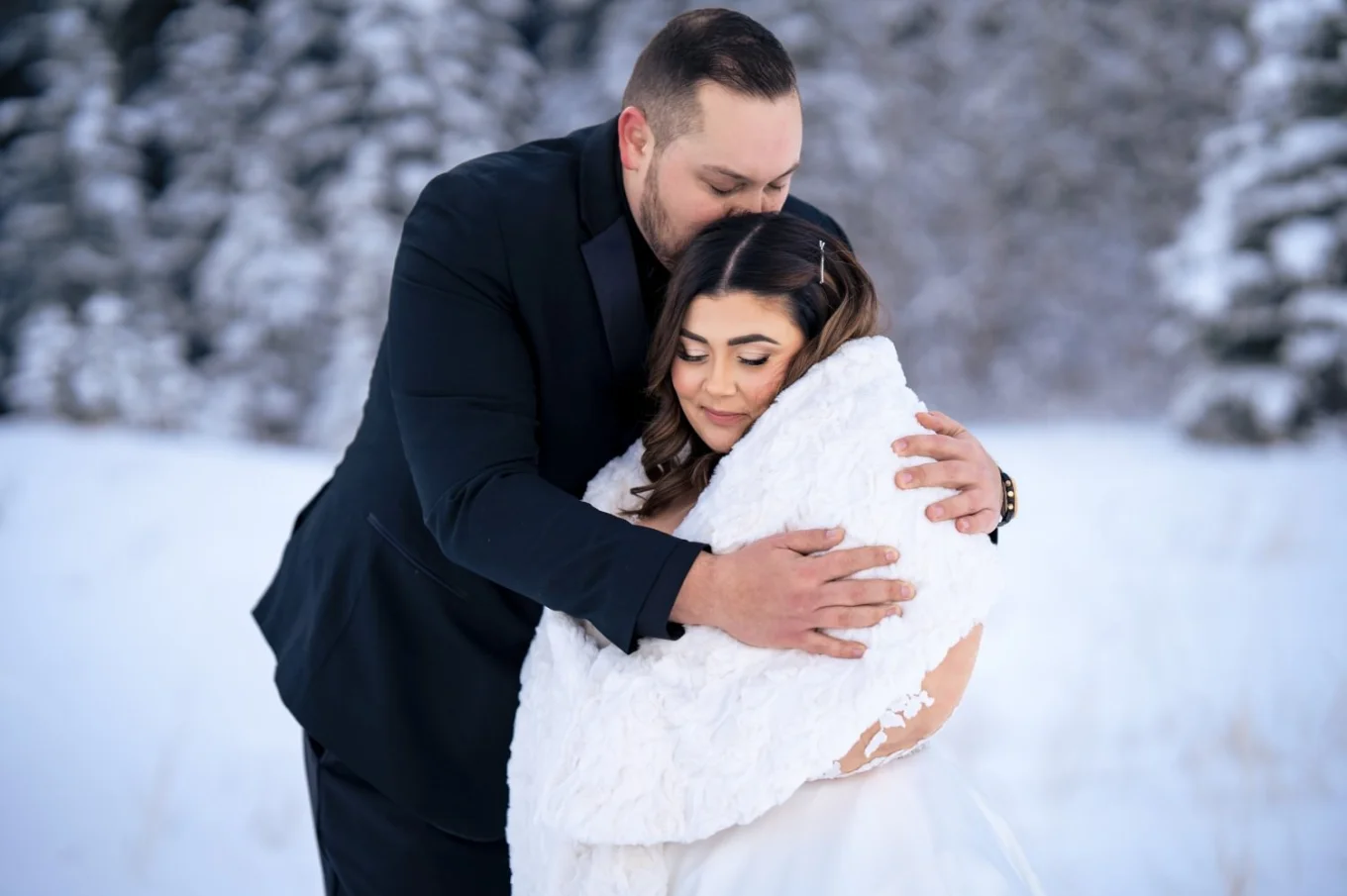 Groom holds his wife in the wintertime in Banff. He protects her from the cold.