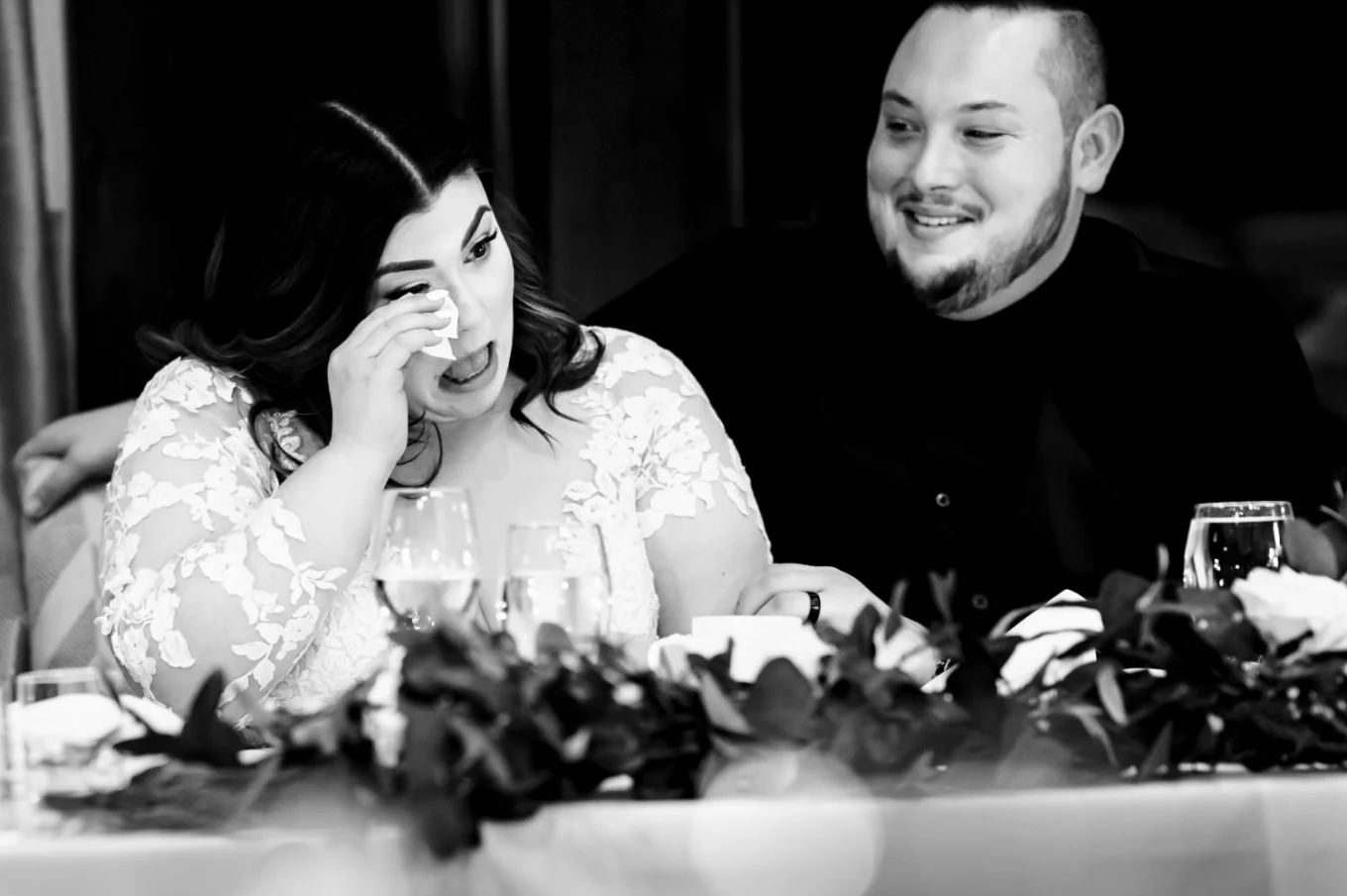 Bride wipes her tears with the napkin during the touching speeches while the groom look at her.