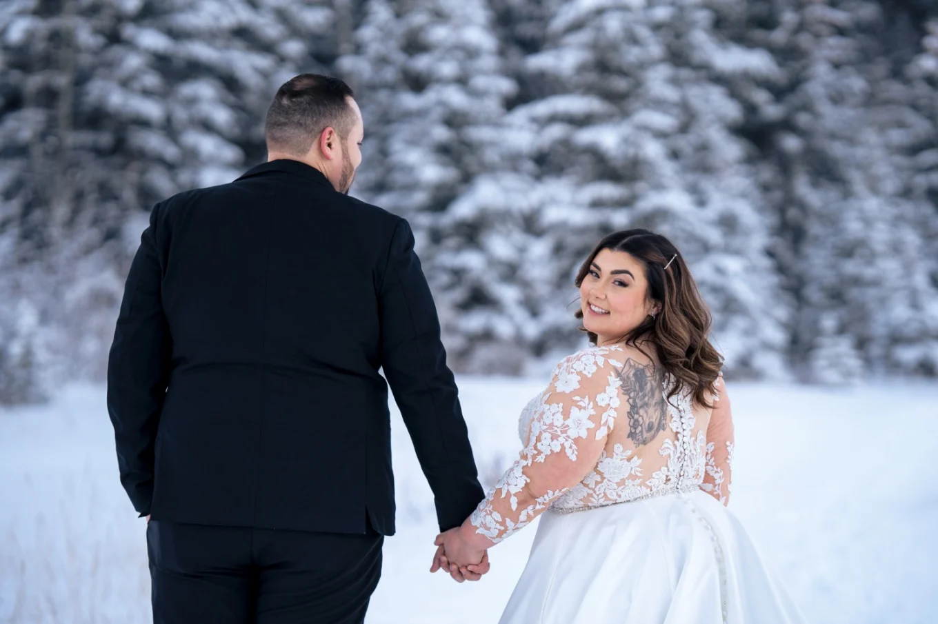 Bride and groom walk in Banff in the winter scenery when the bride look over the shoulder and smiles.