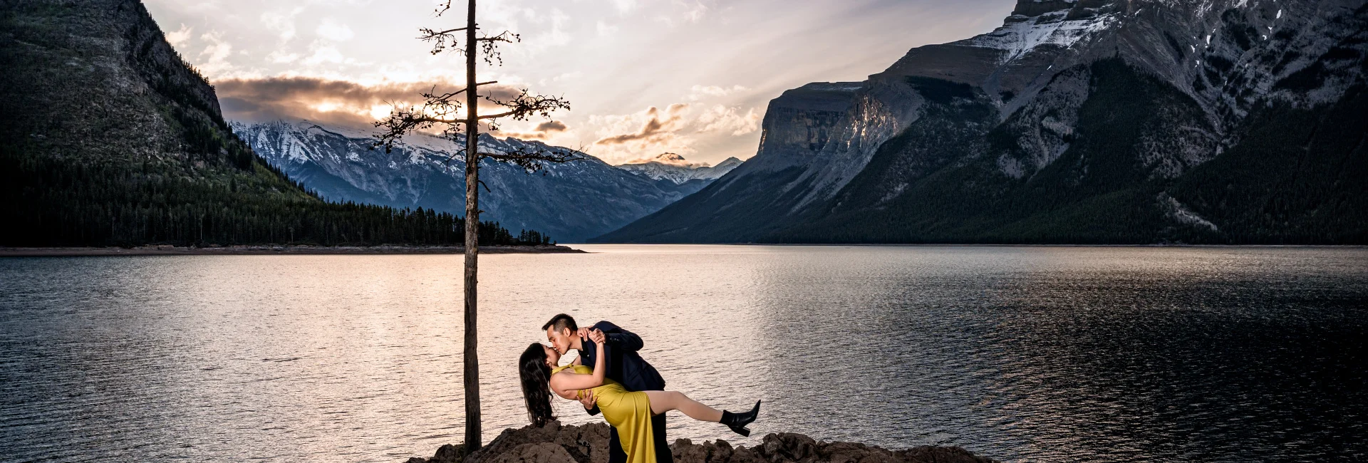 Couple in love dance at Minnewanka Lake during stunning sunrise.