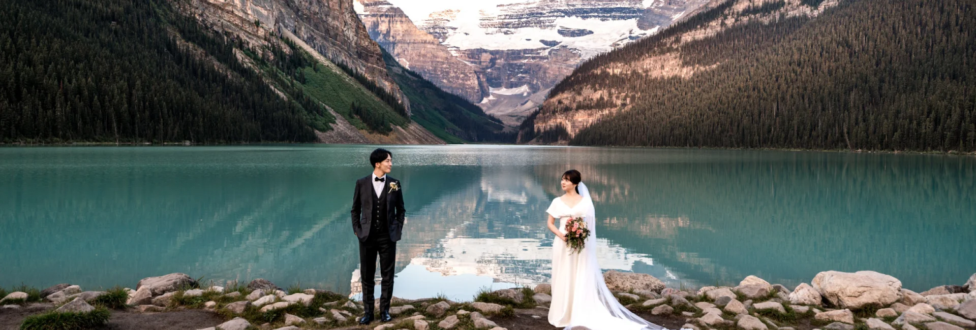 Bride and groom look at each other from a distance at the stunning location of Lake Louise in the Canadian Rockies.
