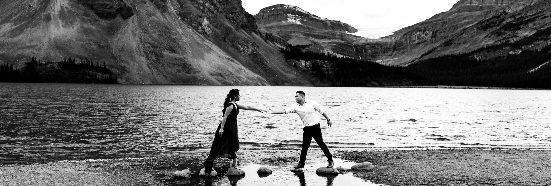 Engaged couple trying to walk on the rocks at Bow Lake during their engagement session