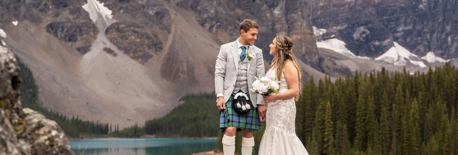 Newlyweds look at each other surrounded by Rocky Mountains at Moraine Lake in Banff.