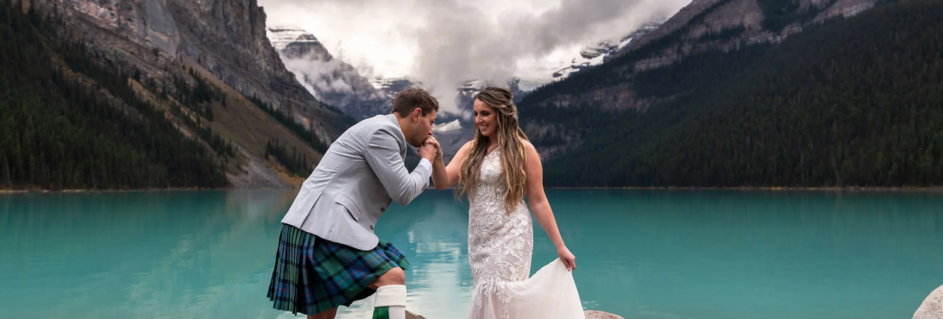Groom kissing the bride's hand during elopement ceremony at Lake Louise.