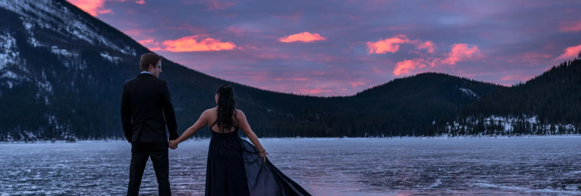 Engaged couple is looking at the red sunrise in the mountains. Engagement photo session in Banff.