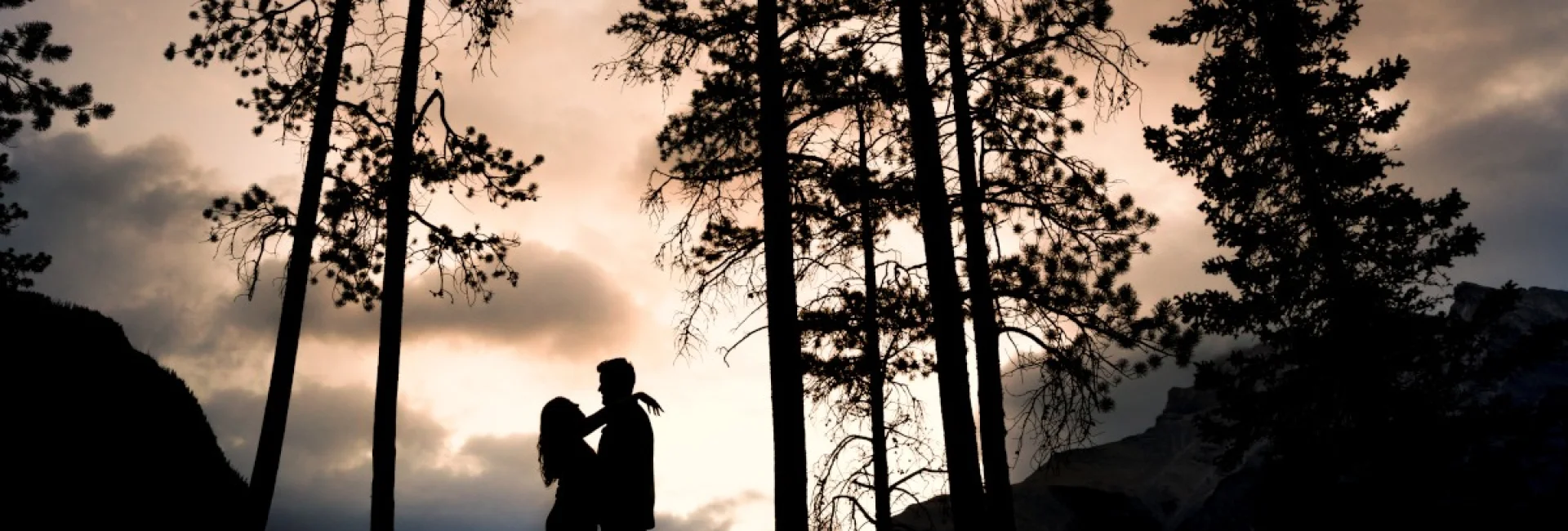 Engaged couple look at each other at Minnewanka Lake during the sunrise